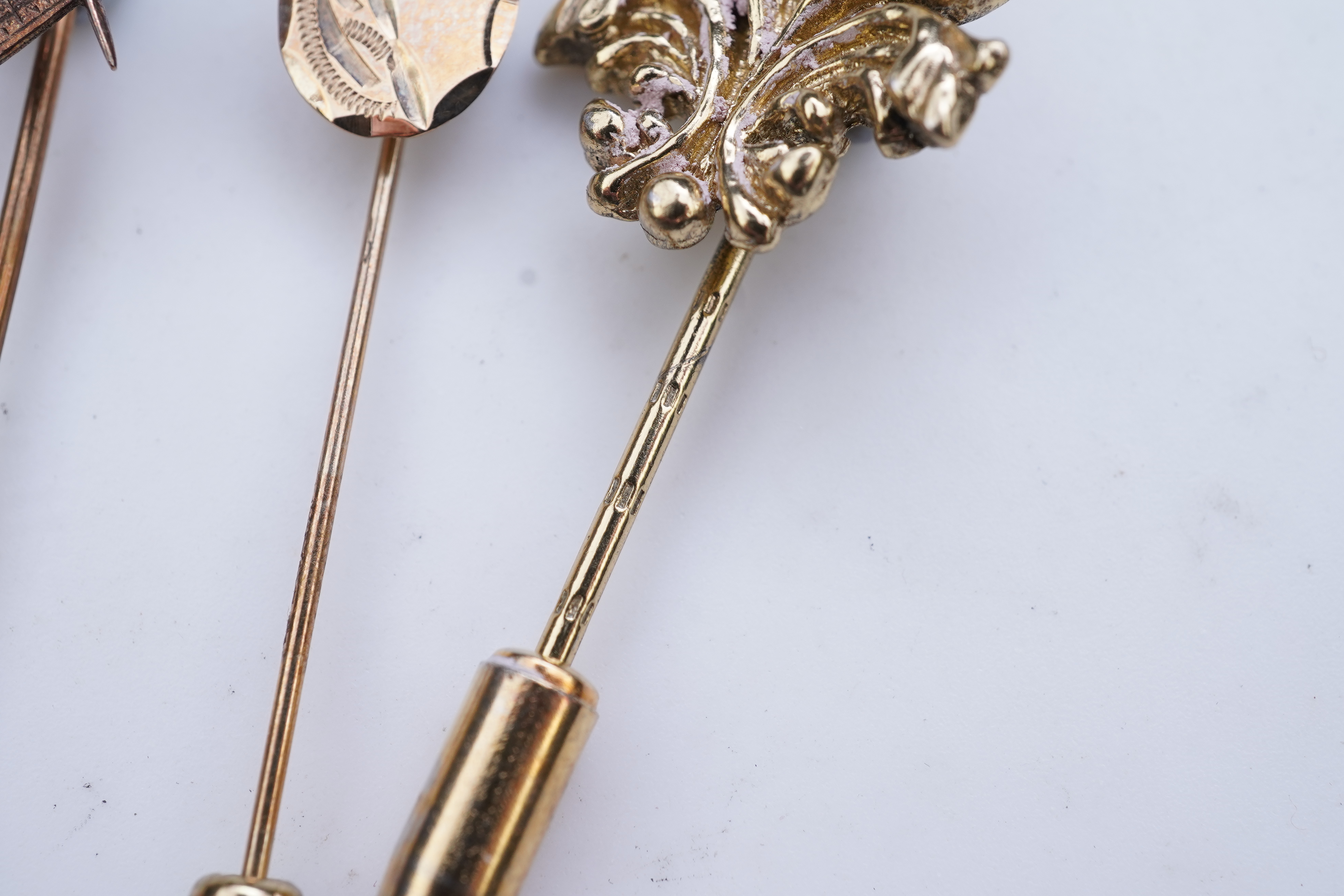 A collection of six stick pins, comprising: three gold stick pins, one set with a hardstone cameo, Austrian assay marks; a gold stick pin with a faceted edge; and a gold stick pin of Masonic design, stamped 9CT, combined